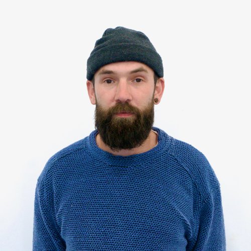 A headshot image of a man wearing a black hat and blue jumper.