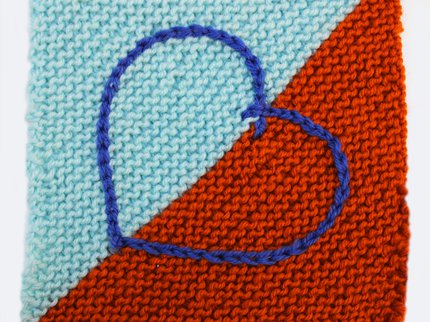A picture of a knitted square with an embroidered heart motif worked in chain stitch