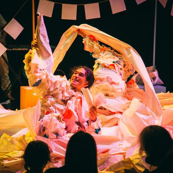 A performer on stage surrounded by origami paper.