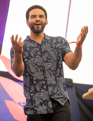 Alex Wharton, poet, stands arms outstretched, smiling.