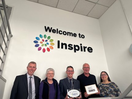 5 smiling  Inspire board members under the Inspire logo sign, 2 holding awards