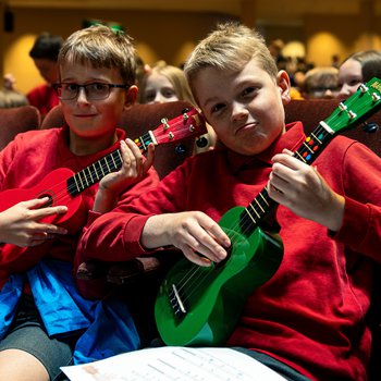 Two boys in red school uniform playing colourful guitars