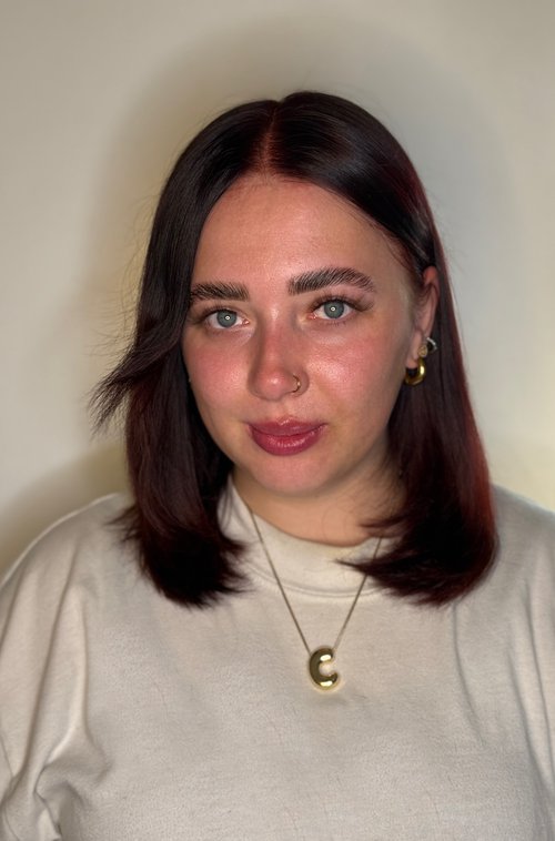 A headshot of a young woman with shoulder length red hair wearing a white t shirt.