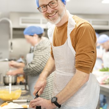 Male adult in teaching kitchen smiling while preparing food