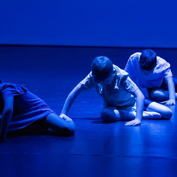 Three children sat on the floor of a stage.