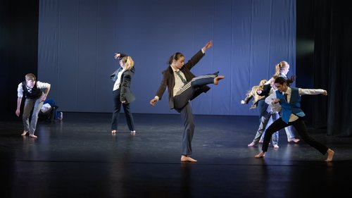 Six young dancers on stage. The front dancer is kicking her right leg in to the air.