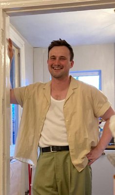 Photograph of Poet Chris Lanyon, a smiling white man with short dark hair and a nose piercing.