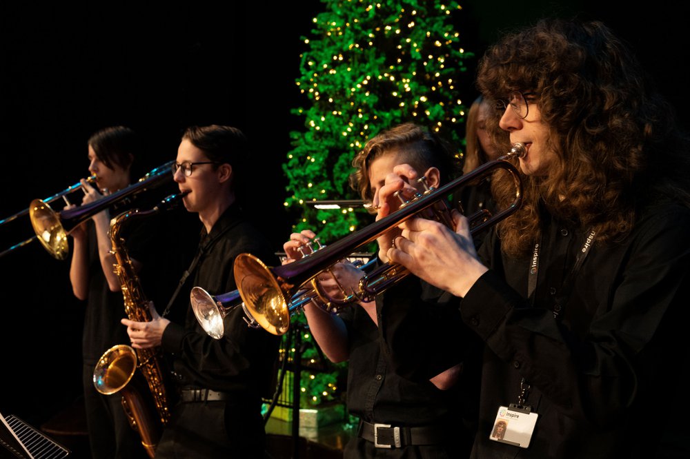 Three musicians playing the trumpet with a christmas tree behind them