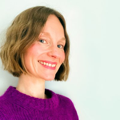 A photo of author and illustrator Claire Powell - a white woman with dark blonde hair cut into a bob, she is wearing a purple jumper.