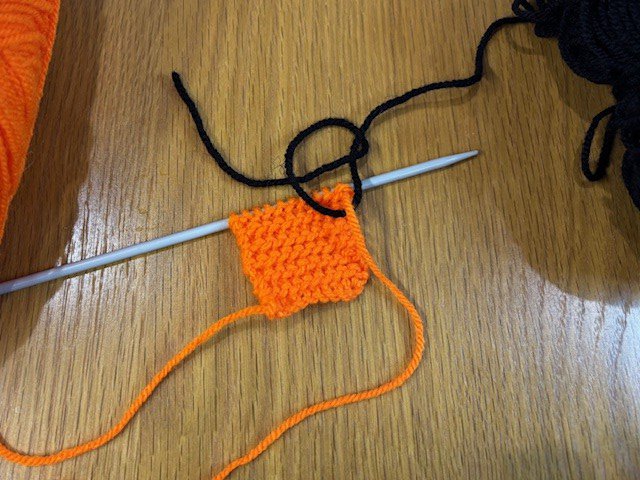A piece of black yarn being tied on to a piece of orange yarn