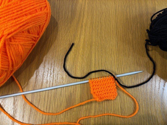 A piece of black yarn being tied on to a piece of orange yarn