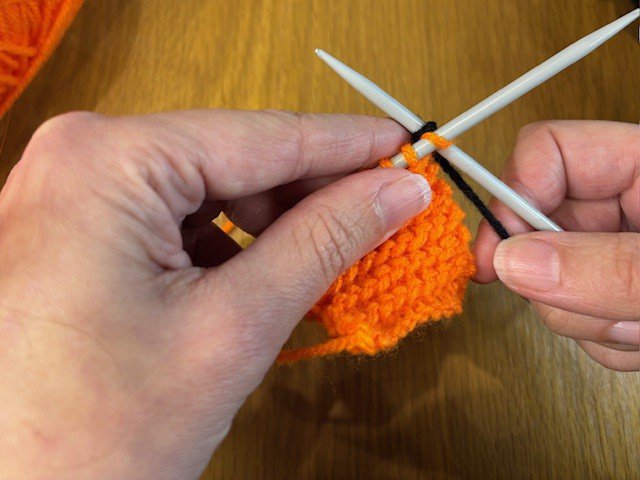Knitting a line of black wool onto a piece of orange knitting
