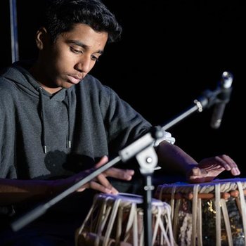 A boy wearing a black hoodie playing the drums.