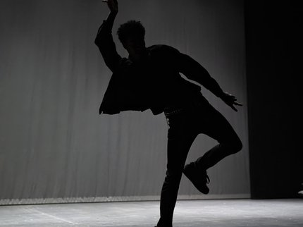A shadow of a boy dancing on stage with one arm and one leg raised.