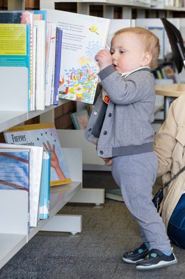 A toddler pulling a picture book from a library shelf