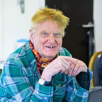 An older white man in a blue checked flannel shirt is smiling at the camera.