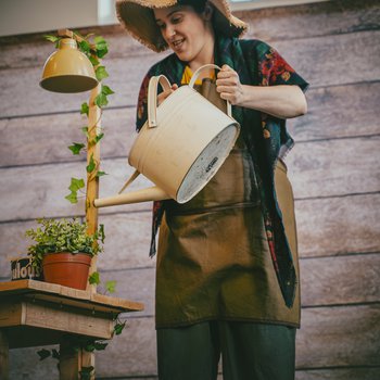 Along Came a Magpie character wearing a hat and watering plants with a watering can.