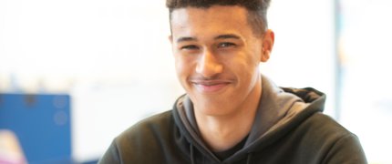 An Inspire College learner, smiling at the camera from his desk.