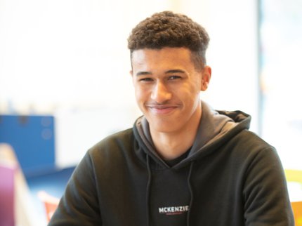 An Inspire College learner, smiling at the camera from his desk.