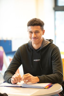 An Inspire College learner, smiling at the camera from his desk.