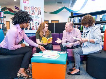 A group of people sit in the library talking and holding books