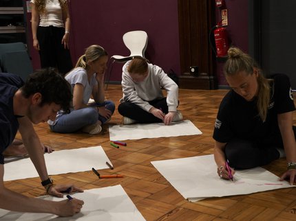 Four young people sat on the floor drawing on large sheets of paper.