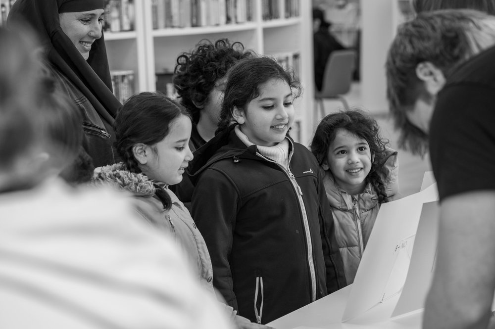 A group of girls smiling, watching an unseen experiment on a table - image is in black and white.