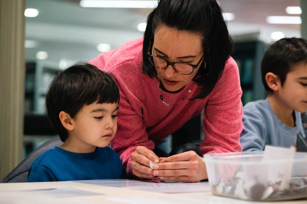 A child in a blue top looking at a small metal object a woman in a pink top is showing him.