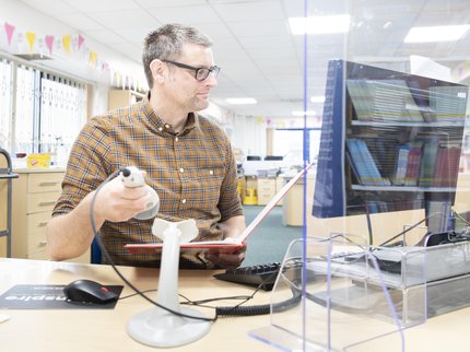 A ELS librarian scans a book at his work desk computer