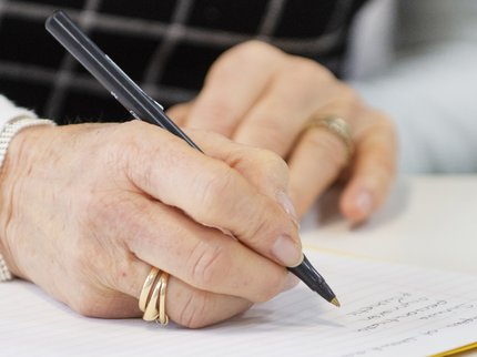 A close up photo of hands as they write in a notepad.