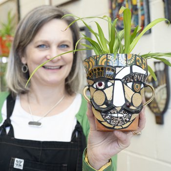 White woman with grey hair holding up her mosaic plant pot