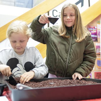 Two girls, one older and one younger, dig in a shallow metal tray