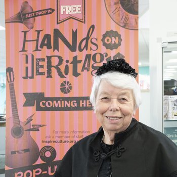 A lady in Victorian costume, standing in front of the banner for Hands on Heritage Day
