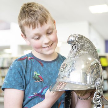 A boy in a blue t-shirt holding a Roman helmet