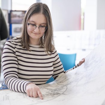 A woman in glasses and a black and white striped t-shirt views a historical map