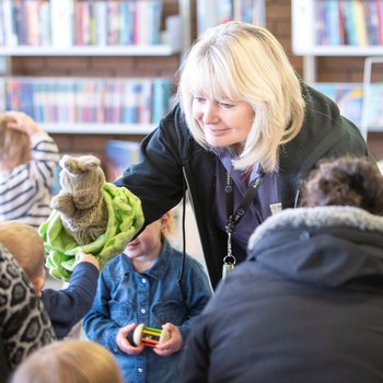 Member of staff holding a Peter Rabbit puppet out to a child