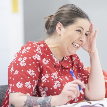 A woman in a red top smiling as she writes something down.