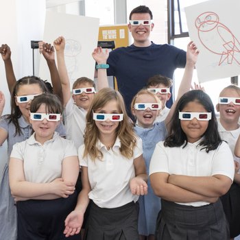 Photograph of artist Pete Gray holding a drawing of an owl, stood behind a group of school children, all wearing 3D glasses