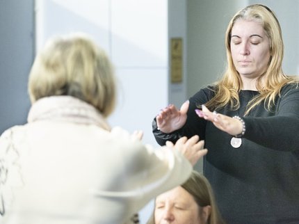 A woman in a white jumper raises her arms with another woman in a black top doing the same with closed eyes
