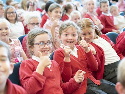 Children in a red school uniform giving a thumbs up