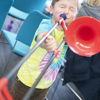 A child wearing a colourful t shirt playing a red trombone.