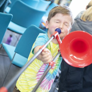 A child wearing a colourful t shirt playing a red trombone.