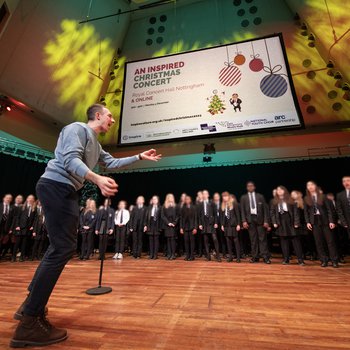 A musician leads a children's choir on stage who are singing