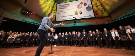 A man conducts on stage while a choir sings