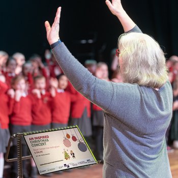 A musical director raises their arms and children sing