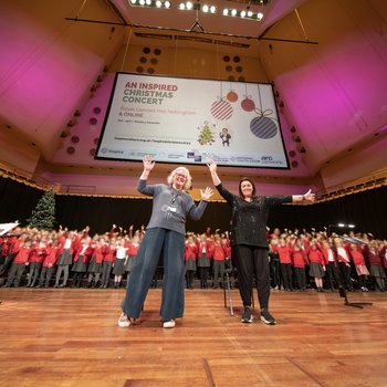 Two school choir leaders smile and raise their hands at the camera