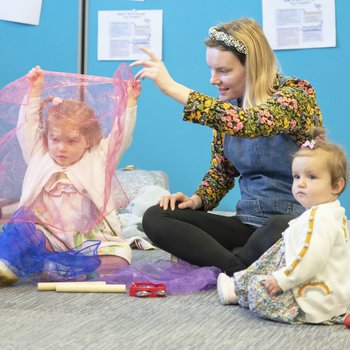 A parent with two young children playing with coloured material.