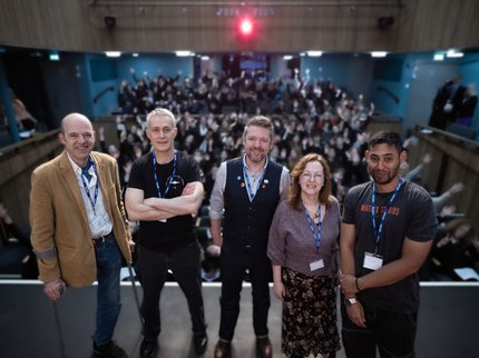 A group of authors stand on a stage and an audience behind