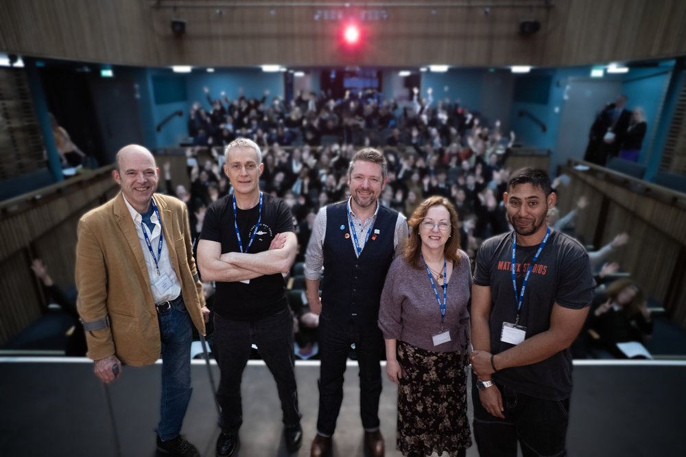A group of authors stand on a stage and an audience behind