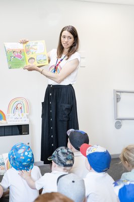 A woman holds up a book and reads to a group of children